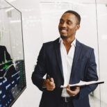 Elegant african man in the office African man in a black suit. Big TV screen. Guy shows presentation.