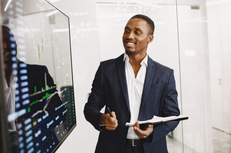 African man in a black suit. Big TV screen. Guy shows presentation.